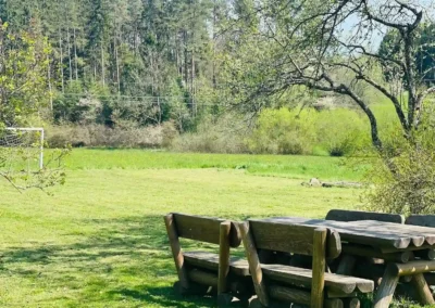Große Wiese mit rustikaler Holzgarnitur und Blick auf Wald und Natur beim Ferienhaus Brestenberg.