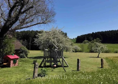 Große Wiese mit Spielturm und blühenden Bäumen in Alleinlage am Ferienhaus Brestenberg.