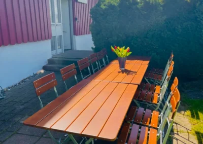 Großer Gartentisch mit Holz-Biergartenstühlen vor dem roten Ferienhaus Brestenberg im Schwarzwald.