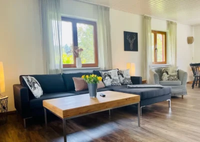 Wohnzimmer im Ferienhaus Brestenberg mit großem Sofa, Couchtisch und hellen Fenstern.