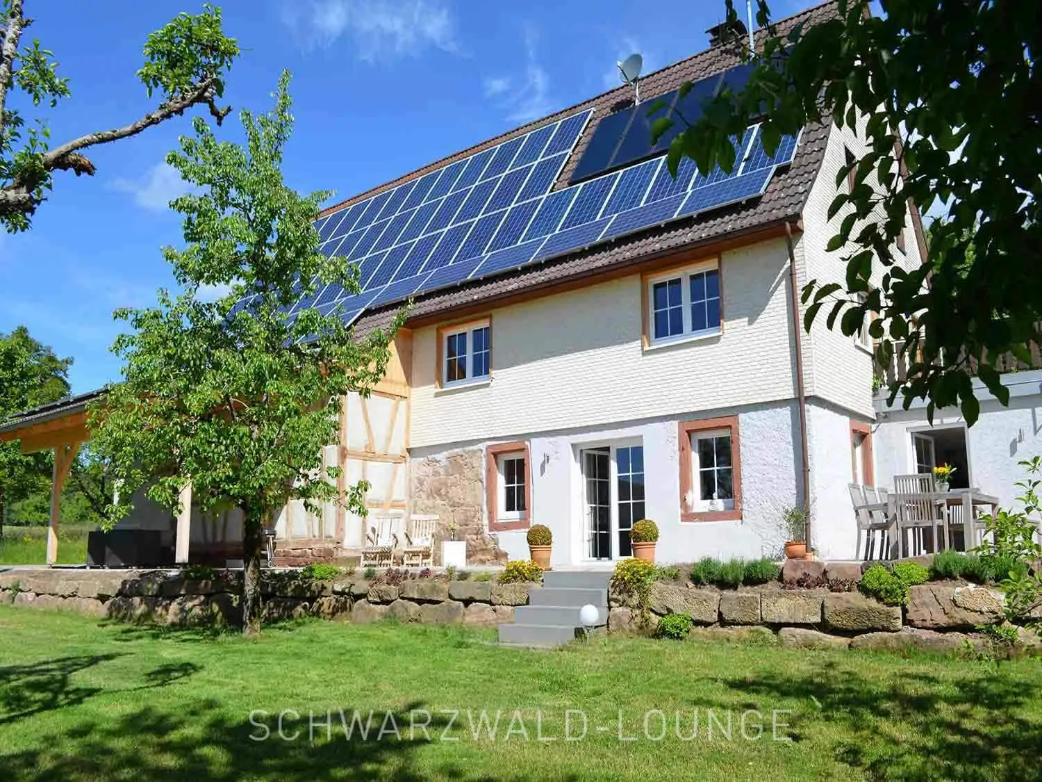 Außenansicht des Chalet Schwarzwald Lindenbuch mit Solaranlage, Fachwerkdetails und großem Garten.