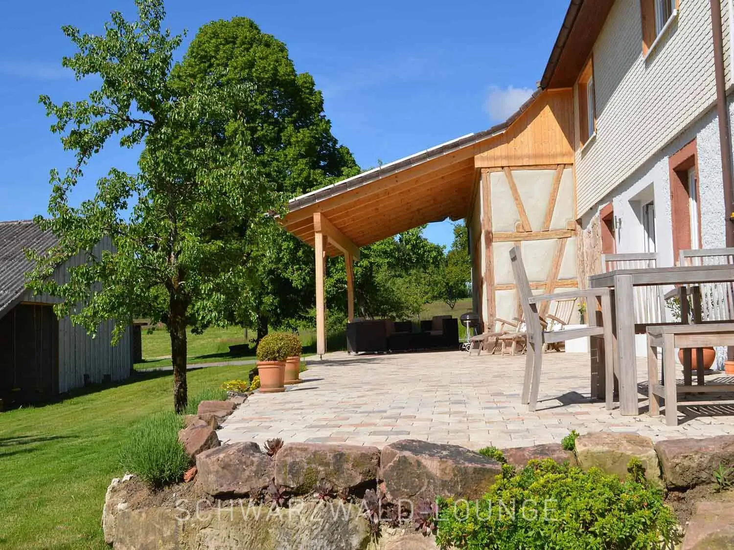 Chalet Schwarzwald – Sonnenterrasse & Naturgarten | Ferienhaus Lindenbuch Seitliche Außenansicht vom Chalet Schwarzwald mit großer Sonnenterrasse und naturbelassenem Garten.