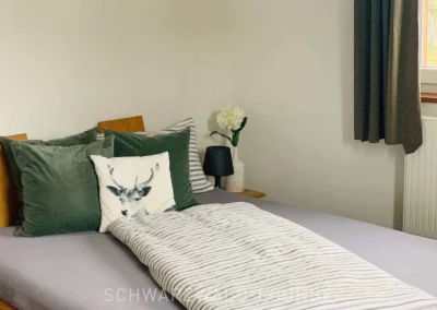 Gemütliches Schlafzimmer im Chalet Schwarzwald Lindenbuch mit grünem Dekokissen, Hirschmotiv und Naturdeko.