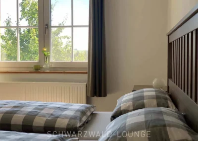 Gemütliches Schlafzimmer im Chalet Schwarzwald mit grauer Bettwäsche und großem Fenster mit Blick ins Grüne.