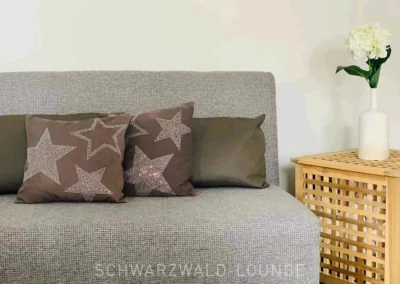 Schlafsofa mit dekorativen Sternkissen im Chalet Schwarzwald Lindenbuch, neben modernem Beistelltisch und Deko-Blumen.