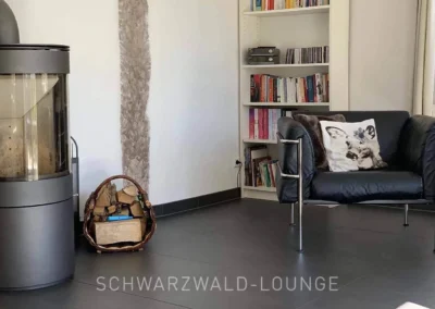 Wohnzimmer mit Kamin, schwarzem Ledersessel und Bücherregal im Chalet Schwarzwald Ferienhaus Lindenbuch