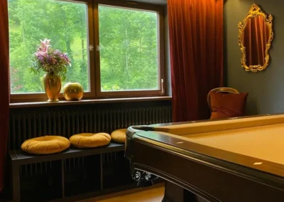 Elegantes Billardzimmer der Gruppenunterkunft Schwarzwald mit Billardtisch, goldenem Spiegel und Sitzmöglichkeiten.