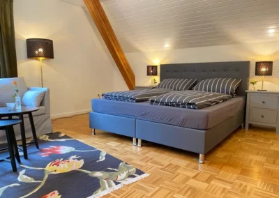 Schlafzimmer mit Boxspringbett, zwei Nachttischen und gemütlichem Loungebereich im Ferienhaus Hof Busems.
