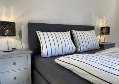 Schlafzimmer mit grauem Doppelbett, passenden Nachttischen und dekorativen Lampen im Ferienhaus Hof Busems.