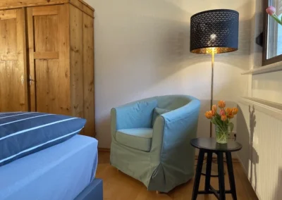 Gemütlicher Sitzbereich im Schlafzimmer mit hellblauem Sessel, Nachttisch und Stehlampe im Ferienhaus Hof Busems.