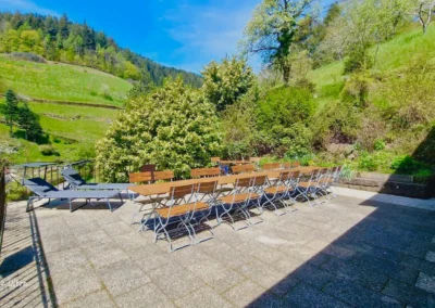 Große Sonnenterrasse mit langen Holztischen, Biergartenstühlen und zwei Liegestühlen mit Blick ins Tal im Ferienhaus Hof Busems.