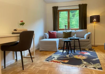 Gemütliche Sitzecke mit hellem Ecksofa, Dekokissen und Schreibtischbereich im Ferienhaus Hof Busems.
