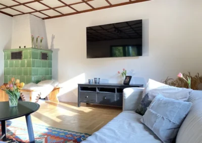 Gemütliches Wohnzimmer mit grünem Kachelofen, großem Fernseher und moderner Sitzecke im Ferienhaus Hof Busems.