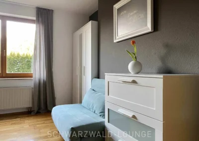 Schlafzimmer der Ferienwohnung Kinzigtal mit Kommode, Sofa und hellen Vorhängen