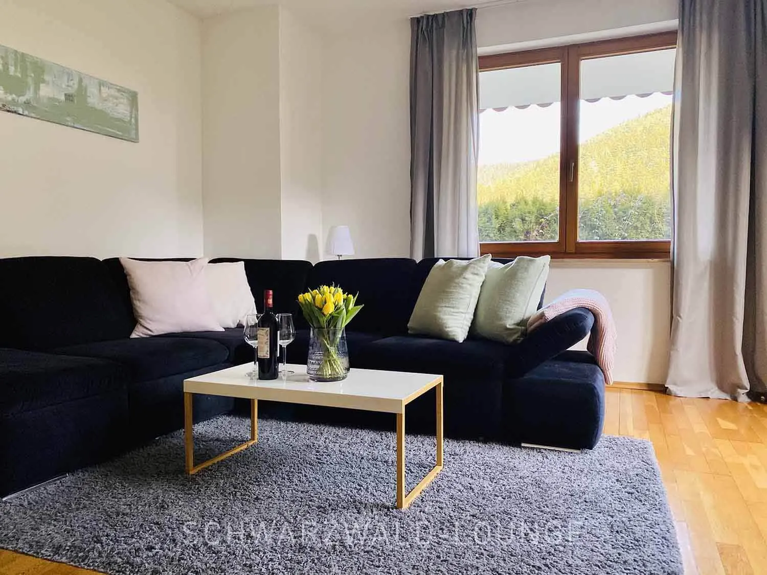 Kinzigtal Schwarzwald – Wohnzimmer mit Sofa & Wein | Blick in den Garten Gemütliches Wohnzimmer der Ferienwohnung Kinzigtal mit Sofa, Wein und Blick in den Garten