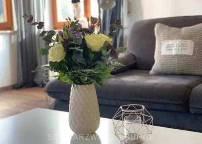 Frischer Blumenstrauß in weißer Vase auf dem Couchtisch im Wohnzimmer der Ferienwohnung Bergsee Schwarzwald.