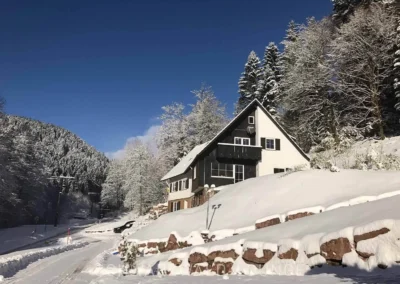 Schwarzwald Chalet Lohmühle im Winter mit verschneiter Landschaft und blauem Himmel.