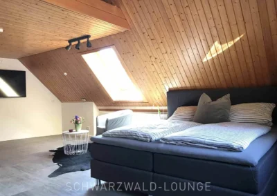 Großzügiges Schlafzimmer mit Boxspringbett, TV und Dachschräge im Schwarzwald Chalet Lohmühle.