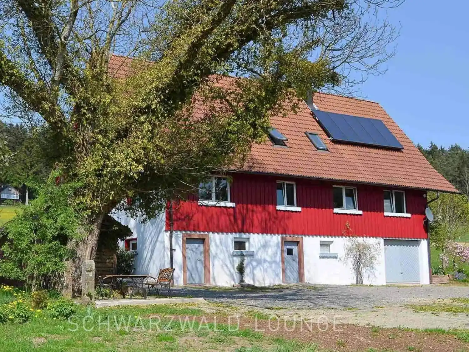Außenansicht des Ferienhauses Brestenberg mit großem Garten, Spielplatz und altem Baum.