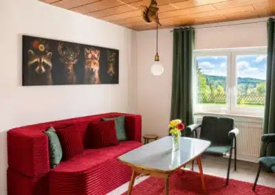 Aufenthaltsraum im Ferienhaus Tanne und Tal Relax mit rotem Sofa, Sesseln und Blick in den Schwarzwald