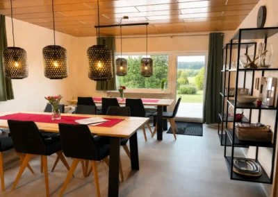 Essbereich im Ferienhaus Tanne und Tal Relax mit Holztischen, schwarzen Stühlen und Blick ins Grüne