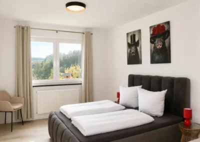 Schlafzimmer im Ferienhaus Tanne und Tal Relax mit Doppelbett, weißen Bettdecken, Sitzplatz und Blick in den Schwarzwald