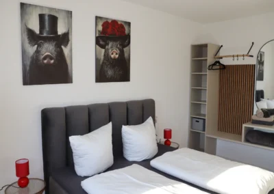 Schlafzimmer im Ferienhaus Tanne und Tal Relax mit Doppelbett, weißen Kissen, roten Lampen und Garderobenbereich
