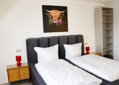 Schlafzimmer im Ferienhaus Tanne und Tal Relax mit Doppelbett, weißen Kissen, Nachttischen und roten Lampen
