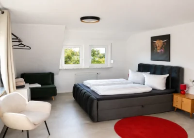 Schlafzimmer im Ferienhaus Tanne und Tal Relax mit Doppelbett, Sitzbereich, Garderobe und roten Akzenten