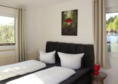 Schlafzimmer im Ferienhaus Tanne und Tal Relax mit Doppelbett, weißen Bettdecken, zwei Fenstern und Blick ins Grüne