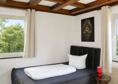 Schlafzimmer im Ferienhaus Tanne und Tal Relax mit Einzelbett, hellen Vorhängen und Blick ins Grüne